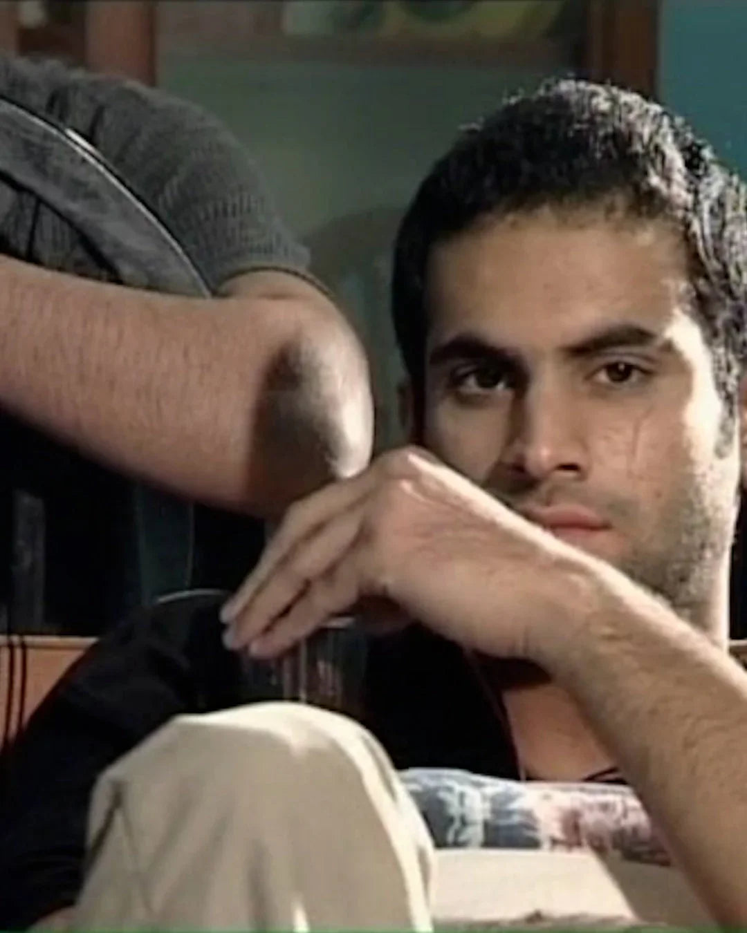 Man with short dark hair sitting indoors, holding a glass, archival Khajistan image