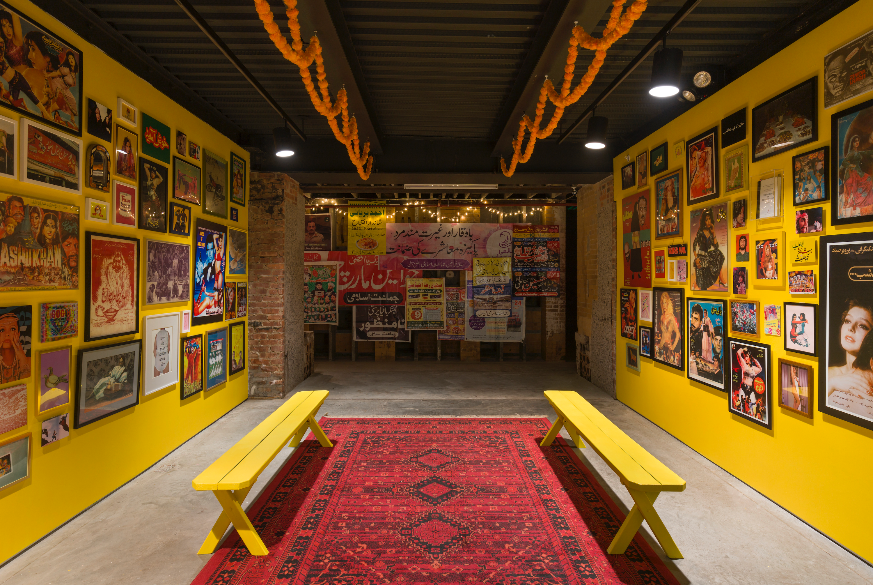 Khajistan gallery with yellow walls, vintage South Asian posters, red rug, and yellow benches